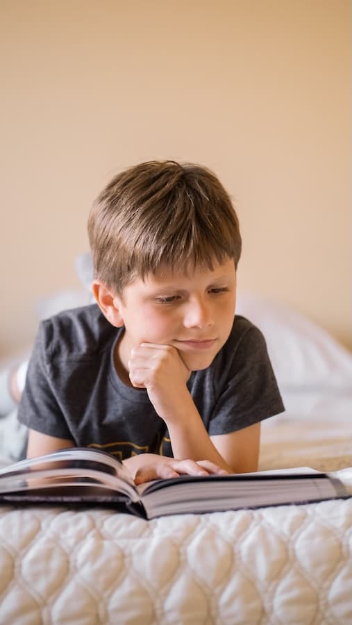 Un enfant est allongé sur un lit et regarde un livre ouvert.
